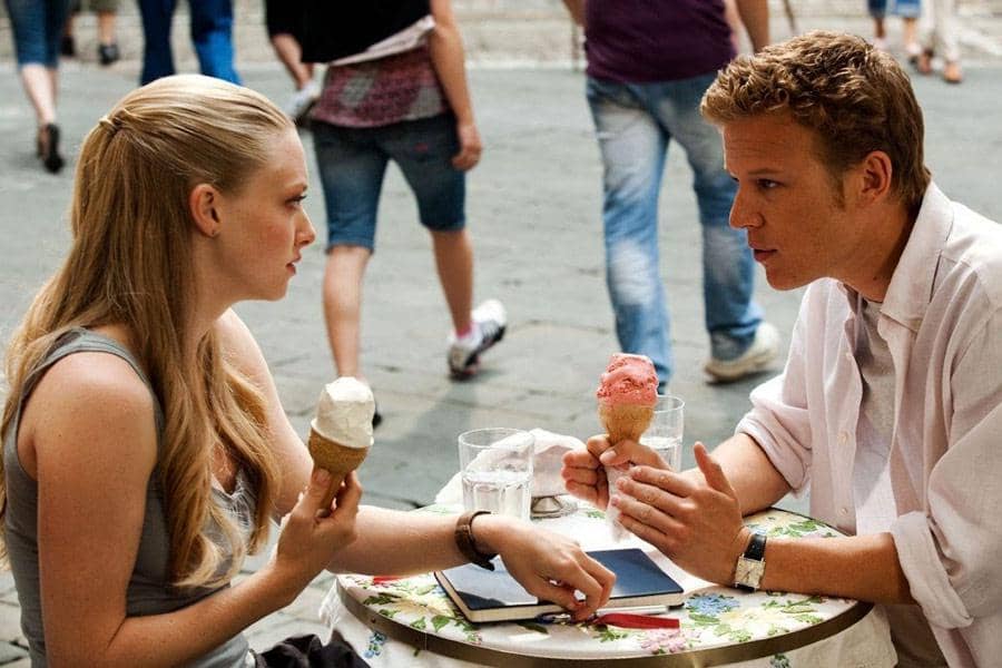 Dua orang duduk di meja kafe luar ruangan sambil menikmati es krim dan berbincang serius di cuplikan film Letters to Juliet.