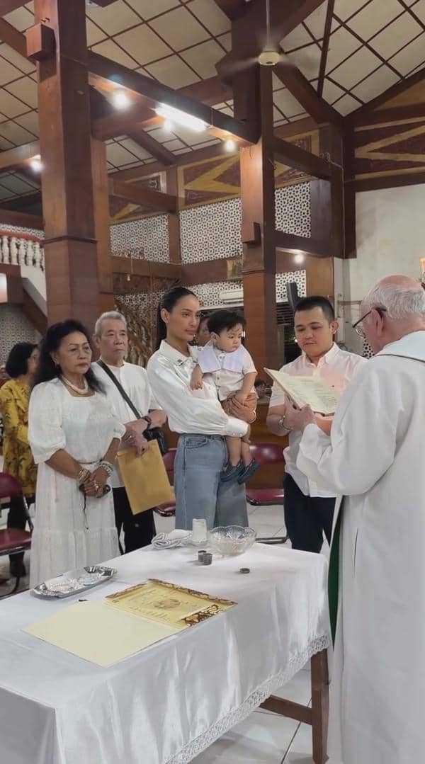 Seorang bayi digendong ibunya saat prosesi pembaptisan di gereja bersama keluarga dan seorang pastor yang memimpin upacara.