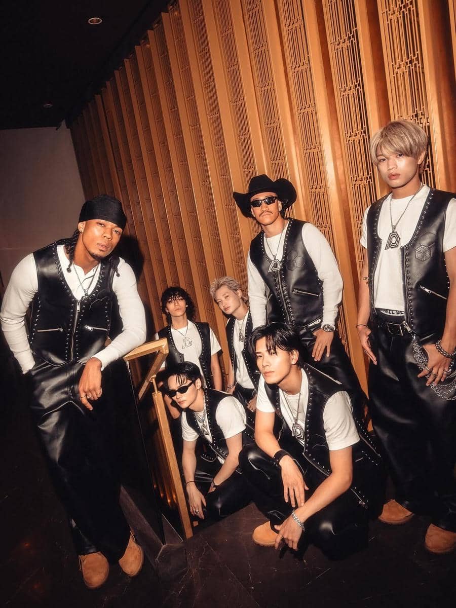 Tujuh personel boy band Jepang PSYCHIC FEVER berpose bersama mengenakan busana kulit hitam dan kaus putih di depan dinding kayu.