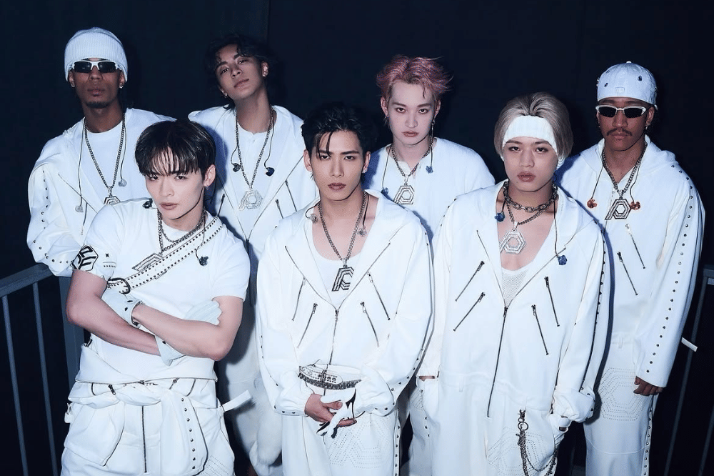 Tujuh personel boy band Jepang PSYCHIC FEVER berpose bersama mengenakan busana serba putih dengan aksesori perak di latar gelap.