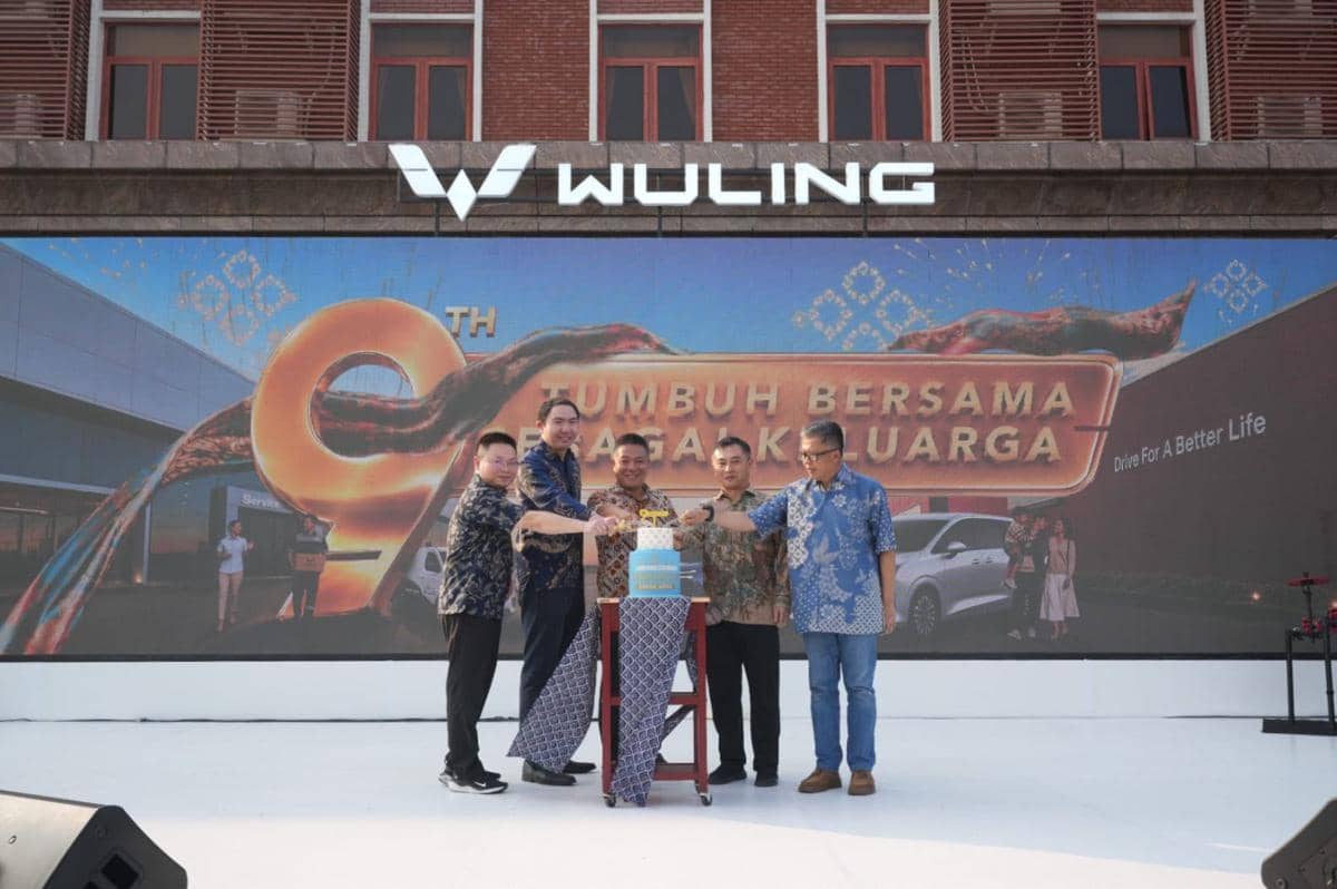 Beberapa pria berdiri di depan panggung dengan latar belakang logo Wuling dan tulisan perayaan ulang tahun ke-9 perusahaan otomotif.