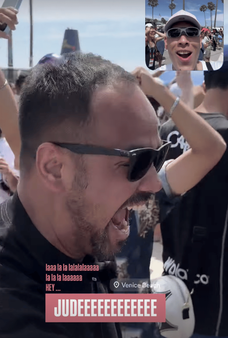 Seorang pria mengenakan kacamata hitam berteriak dengan ekspresi gembira di tengah kerumunan di Venice Beach, dengan inset video kecil di pojok kanan atas memperlihatkan pria lain tersenyum.
