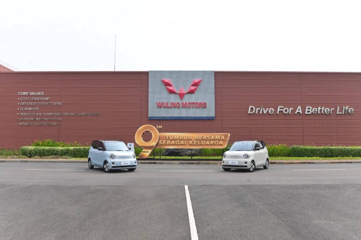 Dua mobil listrik Wuling Air EV diparkir di depan gedung Wuling Motors dengan logo besar dan slogan Drive For A Better Life.