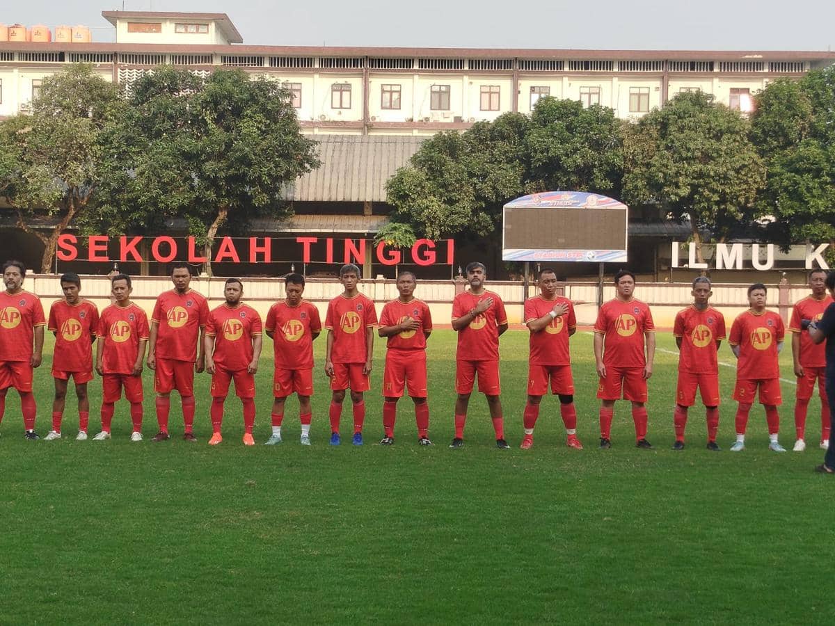 Tim sepak bola Inkracht Sakti FC mengenakan seragam merah berbaris di lapangan sebelum pertandingan uji coba di depan gedung bertuliskan Sekolah Tinggi.