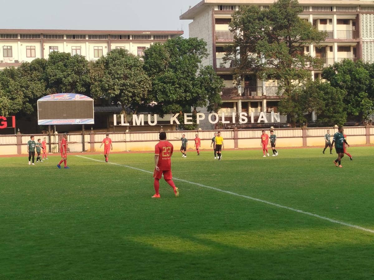 Pemain Inkracht Sakti FC mengenakan seragam merah saat menjalani laga uji coba di lapangan sepak bola dengan latar gedung bertuliskan Ilmu Kepolisian.
