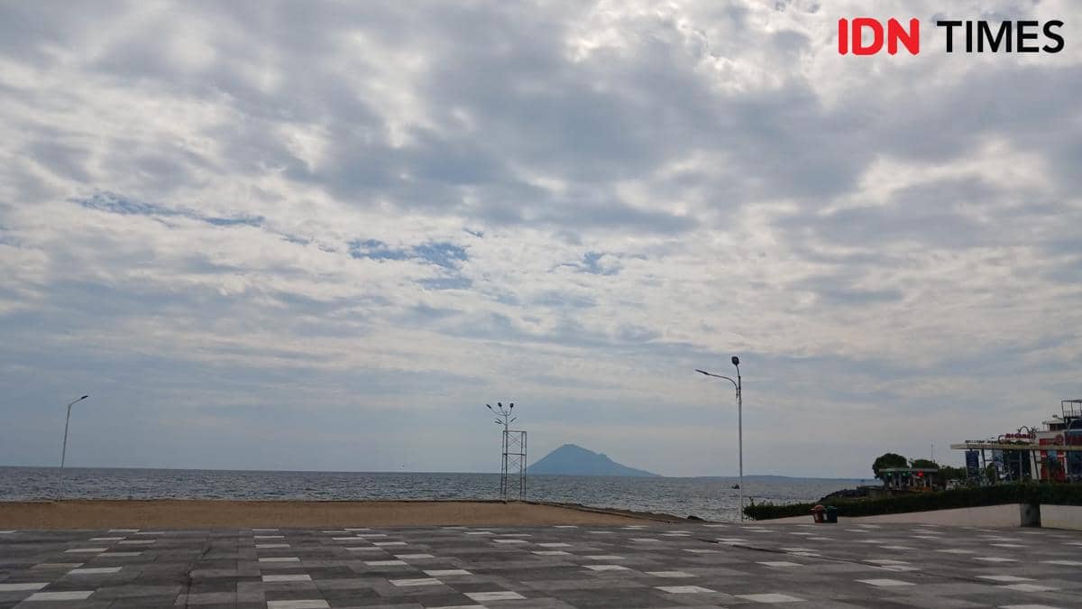 Pemandangan Teluk Manado dengan langit berawan dilihat dari tepi daratan Kota Manado, Sulawesi Utara, dengan laut tenang di kejauhan.