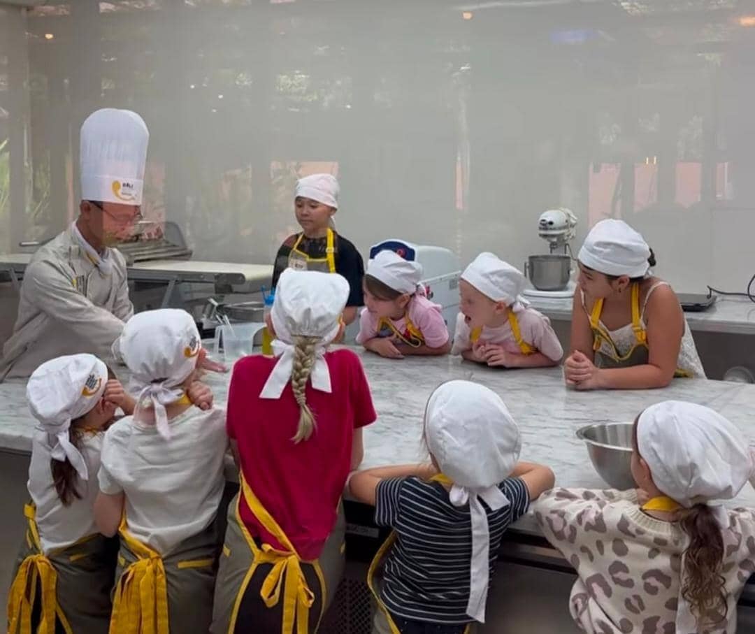 Seorang koki mengajar sekelompok anak-anak yang mengenakan celemek dan topi koki kecil saat mengikuti kelas memasak di Bali.
