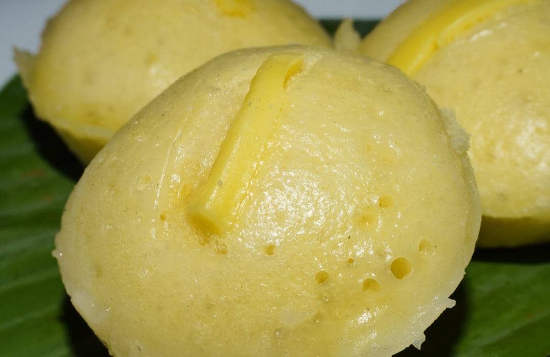Beberapa kue cubit oncom keju berwarna kuning keemasan dengan parutan keju di atasnya disajikan di atas daun pisang.