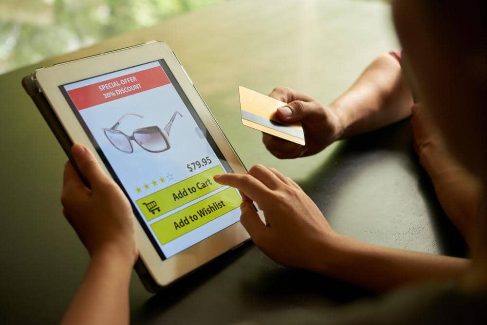 Seseorang berbelanja online menggunakan tablet untuk membeli kacamata dengan kartu kredit di tangan, menampilkan diskon 30 persen.