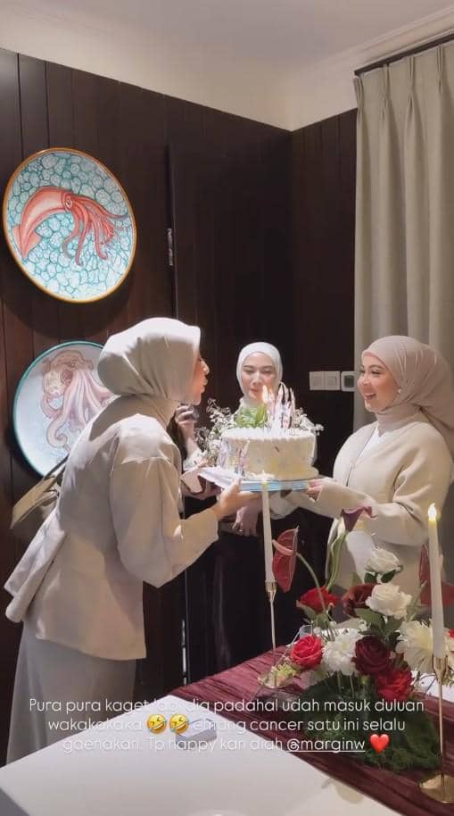 Beberapa wanita berhijab merayakan ulang tahun dengan kue bertabur lilin di meja yang dihiasi bunga mawar merah dan lilin.
