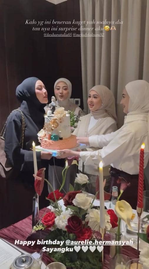 Beberapa wanita berhijab merayakan ulang tahun di sebuah ruangan dengan dekorasi bunga dan lilin, sambil membawa kue bertingkat.