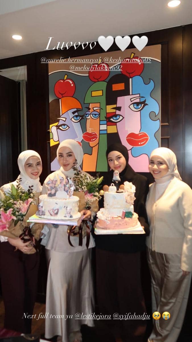 Empat wanita berhijab berpose bersama sambil memegang kue ulang tahun dan buket bunga di depan lukisan bergaya abstrak warna-warni.