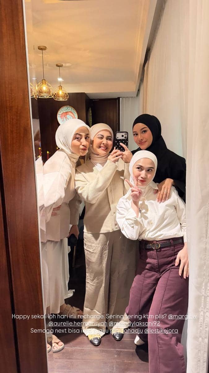 Empat wanita berhijab berpose bersama di depan cermin sambil tersenyum dan berfoto menggunakan ponsel di sebuah ruangan hangat.