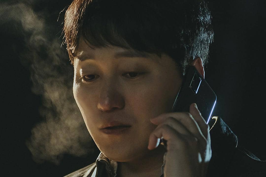 Seorang pria berbicara di telepon di malam hari dengan ekspresi serius, uap napas terlihat di udara dingin.