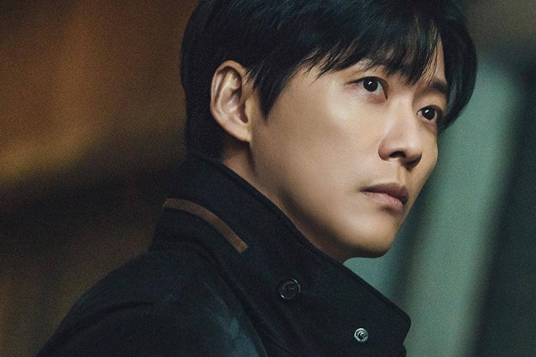 Seorang pria berambut hitam mengenakan jaket gelap menatap serius ke arah samping dalam adegan drama The Husband.