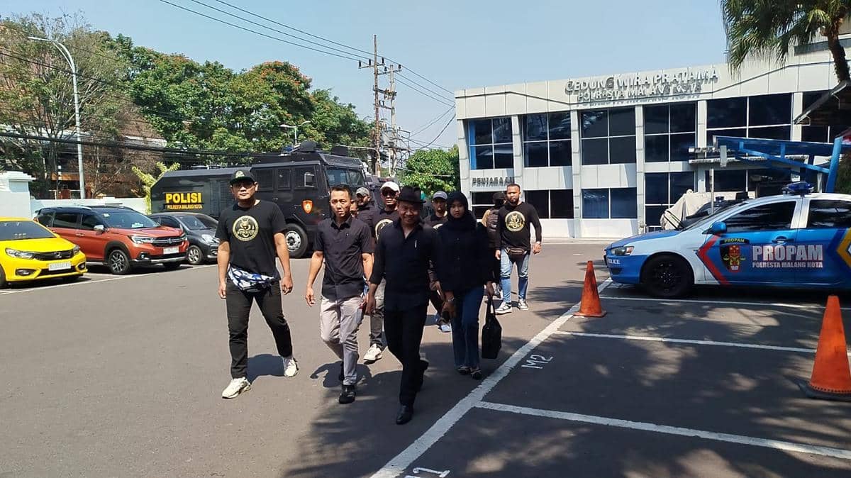 Beberapa orang berjalan di area parkir depan Gedung Wira Pratama Polresta Malang Kota dengan mobil polisi dan kendaraan lain di sekitarnya.