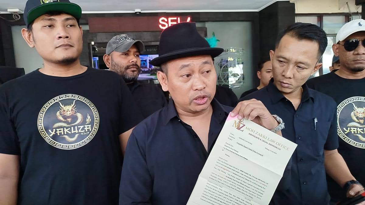 Seorang pria mengenakan topi hitam memegang surat dari kantor hukum, dikelilingi beberapa pria berbaju hitam dengan logo naga bertuliskan Yakuza.