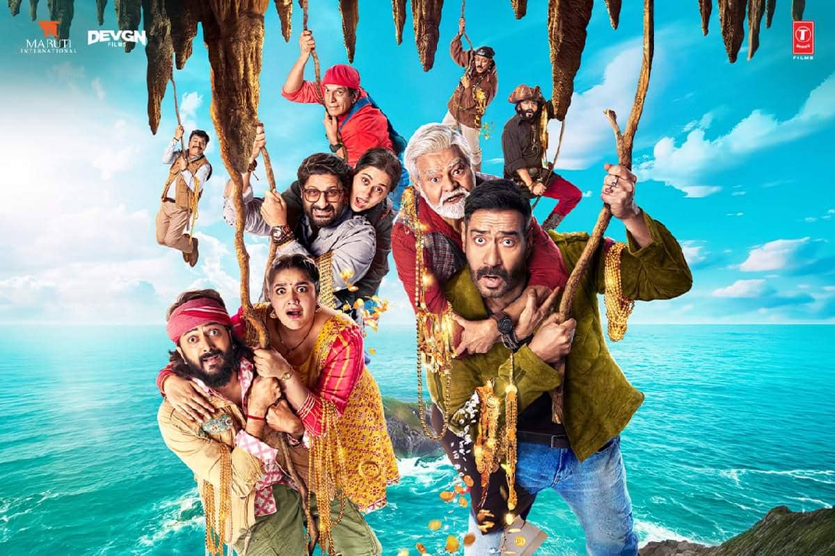 Para pemeran film Dhamaal 4 bergelantungan di tali di tepi tebing dengan latar laut biru dan langit cerah, menampilkan ekspresi kocak dan tegang.