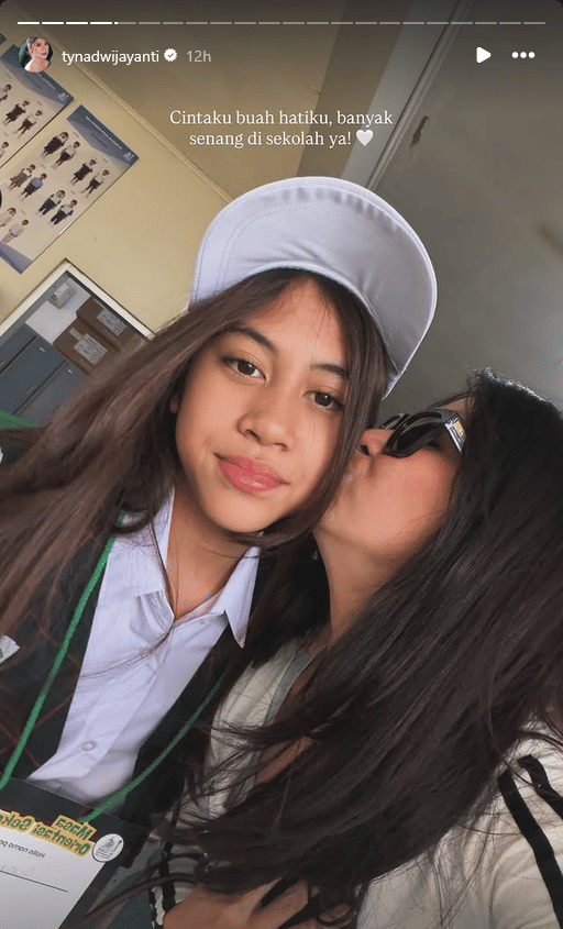 Seorang wanita mencium pipi anak perempuan berseragam sekolah pada hari pertama masuk sekolah tahun 2026 di depan ruang kelas.