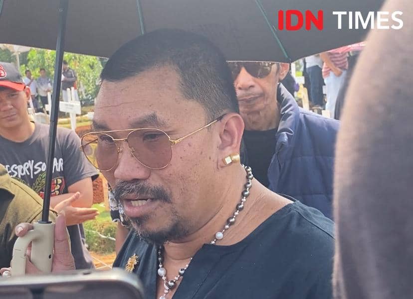 Seorang pria mengenakan kacamata hitam dan kalung mutiara berbicara di bawah payung saat menghadiri pemakaman di TPU Tanah Kusir, Jakarta Selatan.