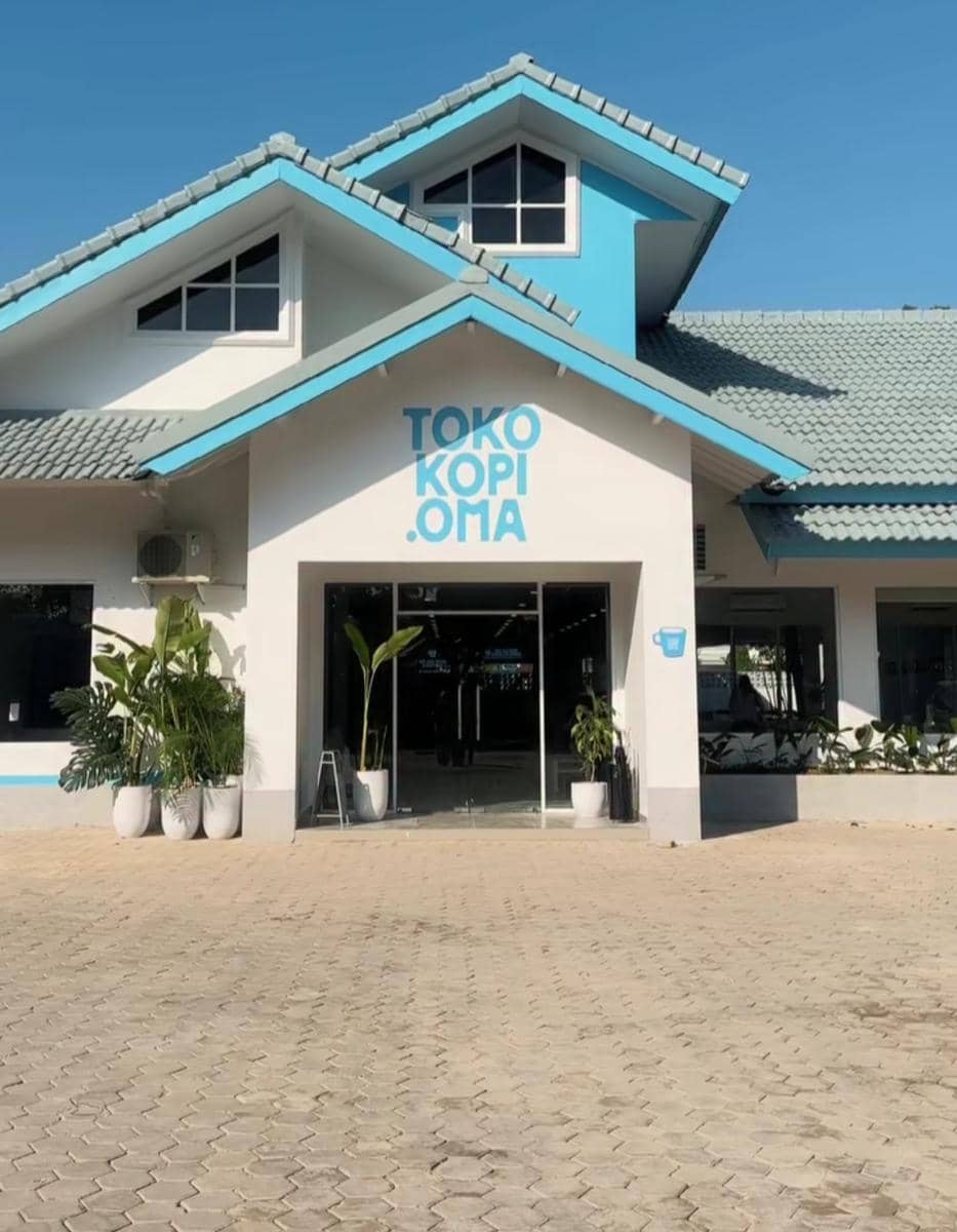 Bangunan cabang baru Toko Kopi Oma di kawasan Way Halim dengan desain modern berwarna putih dan biru di bawah langit cerah.