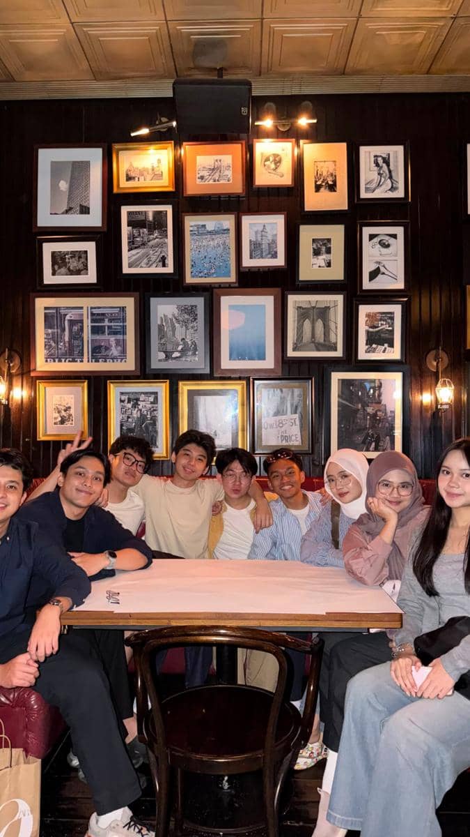 Sekelompok peserta Clash of Champions Season 3 duduk bersama di sebuah kafe dengan dinding penuh bingkai foto hitam putih.