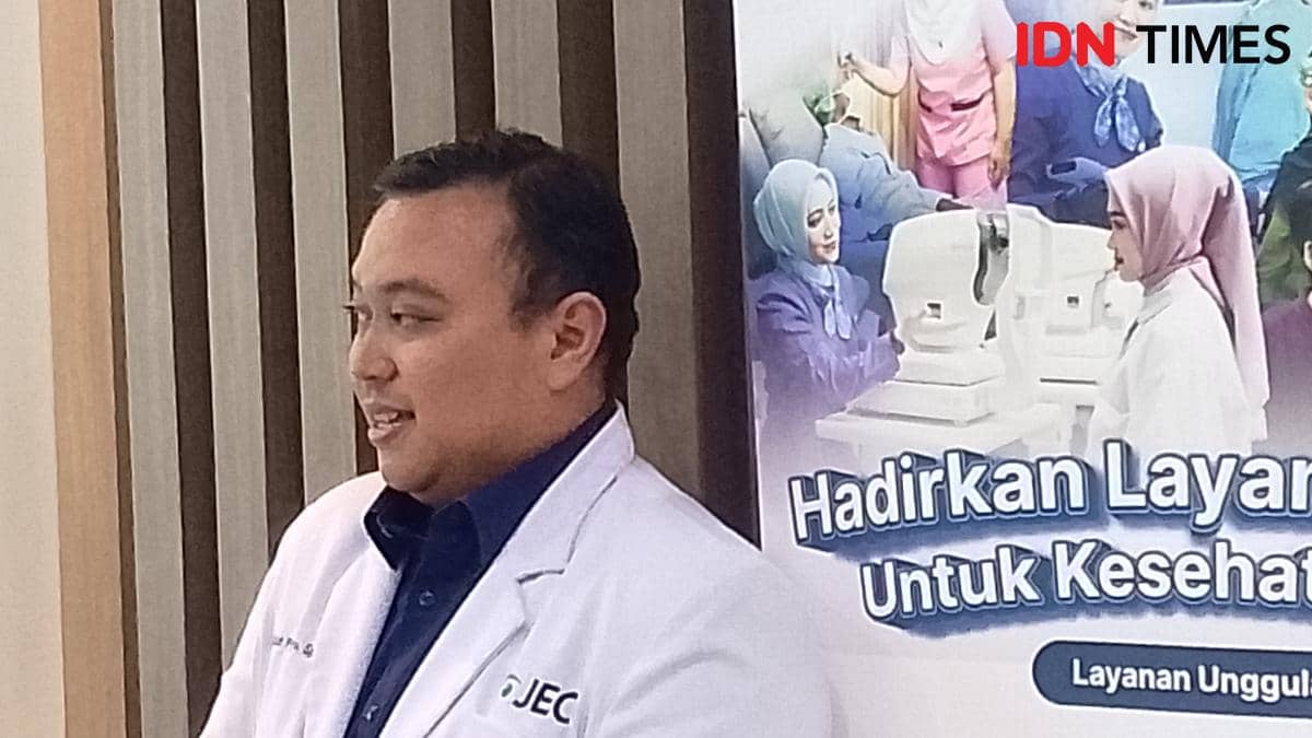 Seorang dokter mengenakan jas putih dengan logo JEC berbicara di depan poster layanan kesehatan mata di Purwokerto.