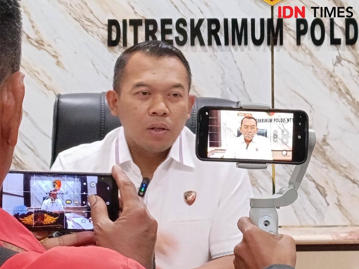 Seorang pejabat kepolisian duduk di depan latar bertuliskan Ditreskrimum Polda NTT saat direkam menggunakan dua ponsel.
