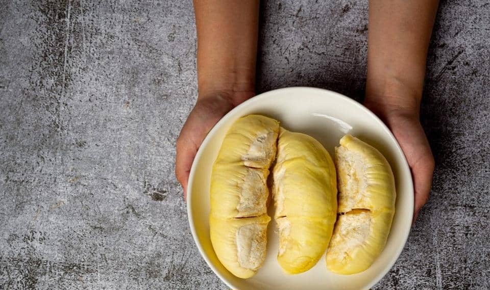 Daging buah durian berwarna kuning pucat tersusun dalam wadah, memperlihatkan tekstur lembut dan tebal.
