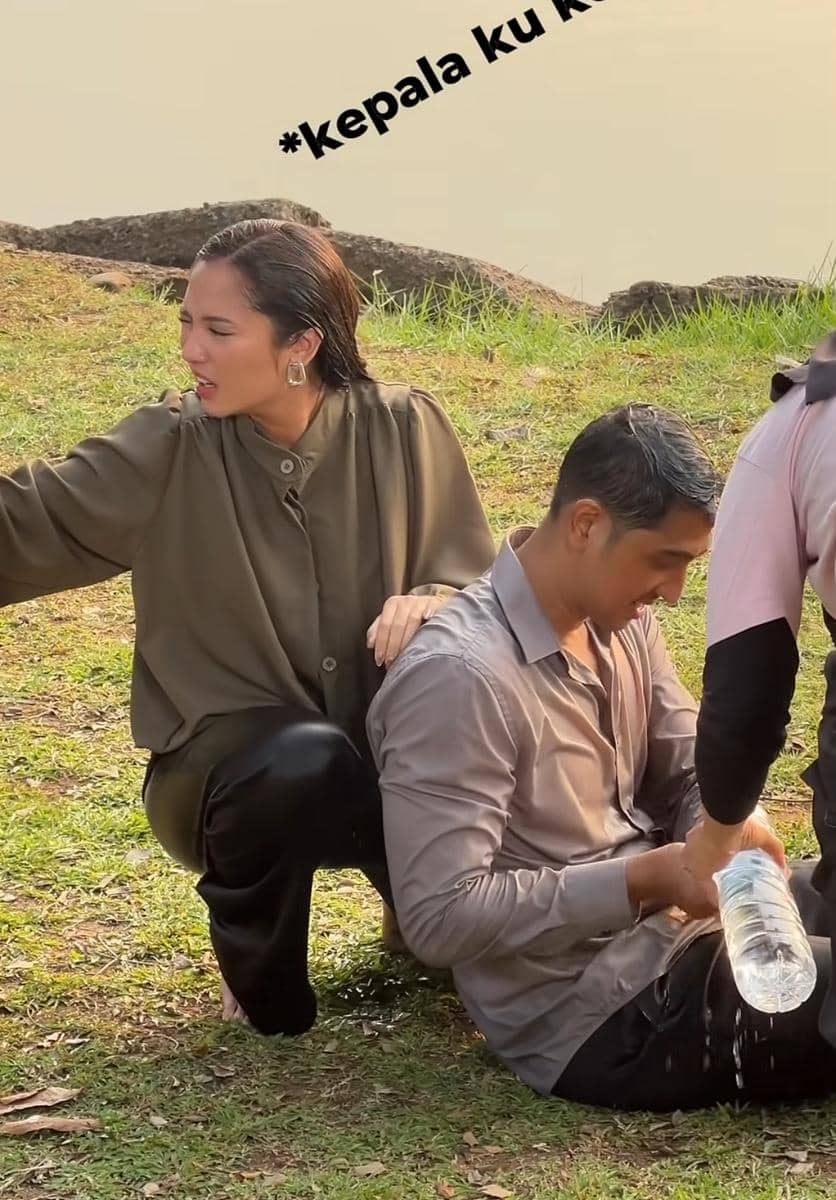Dua pemeran sinetron Terikat Janji duduk di atas rumput dekat danau, salah satunya tampak memegang botol air dan terlihat kelelahan.