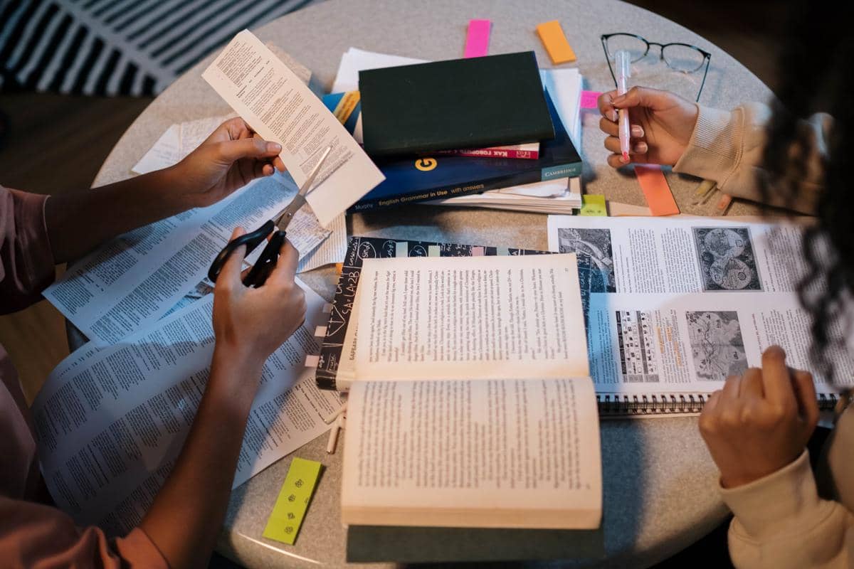 Siswa bekerja sama dalam sebuah proyek menggunakan buku pelajaran dan catatan di meja bulat.