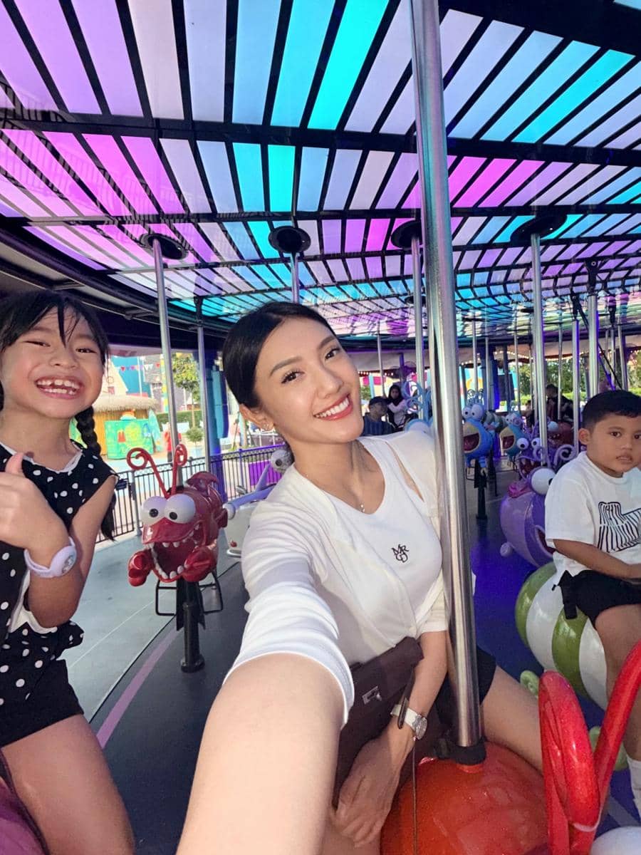 Seorang wanita berpose sambil tersenyum bersama dua anak di wahana permainan berwarna cerah di Universal Studio Singapura.