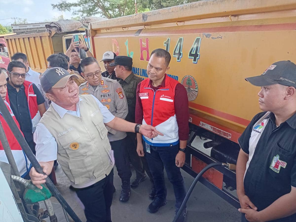 Seorang pejabat daerah bersama petugas dan aparat kepolisian meninjau proses penyaluran bahan bakar minyak di dekat truk tangki.