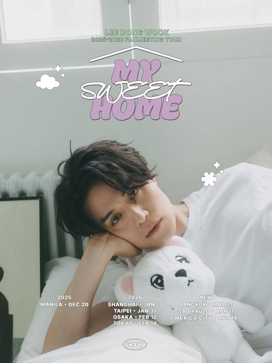 Seorang pria berbaring di tempat tidur sambil memeluk boneka beruang putih dengan tulisan tur penggemar 2025–2026 bertema My Sweet Home.