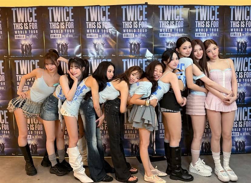 Sembilan anggota grup musik perempuan berpose bersama di depan backdrop bertuliskan 'TWICE This Is For World Tour Finale in Seoul'.