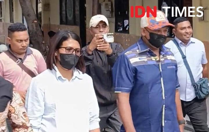 Seorang perempuan dan seorang laki-laki berjalan bersama di luar gedung, keduanya mengenakan masker hitam dan pakaian kasual.