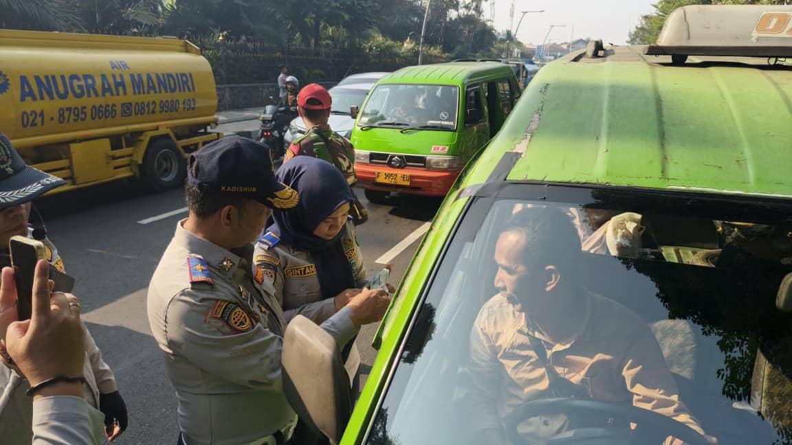 Petugas Dinas Perhubungan memeriksa kelengkapan surat-surat seorang sopir angkot berwarna hijau di pinggir jalan raya.
