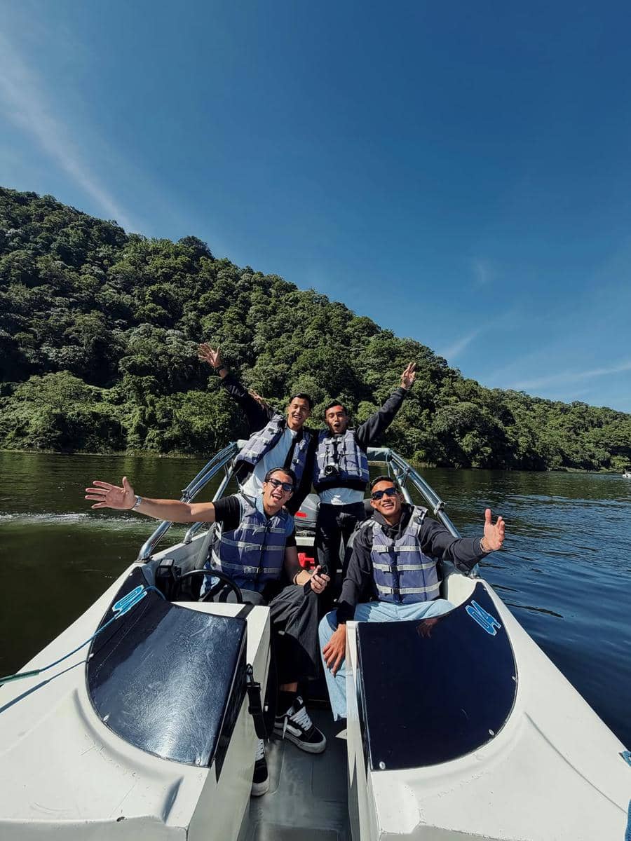 Empat pria mengenakan jaket pelampung berpose ceria di atas perahu motor di danau dengan latar belakang perbukitan hijau di Bali.
