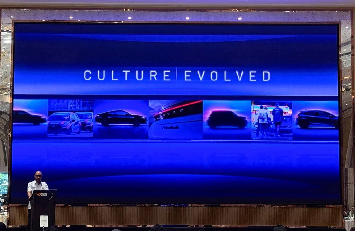 Layar besar bertema 'Culture Evolved' dengan tampilan siluet mobil dan pembicara berdiri di podium dalam acara Honda.