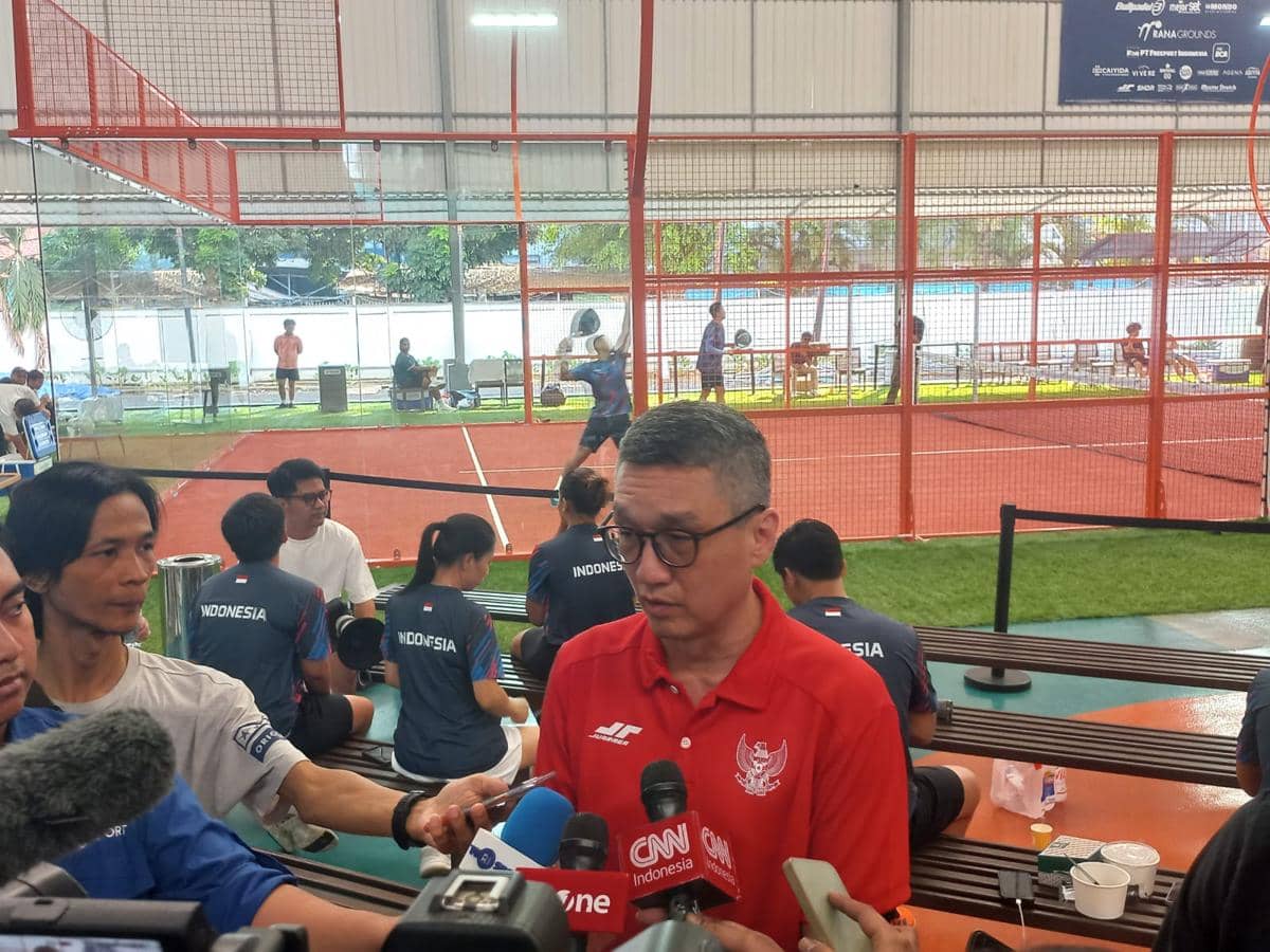 Seorang pelatih Timnas Padel Indonesia mengenakan kaus merah memberikan keterangan kepada media di area lapangan padel indoor.