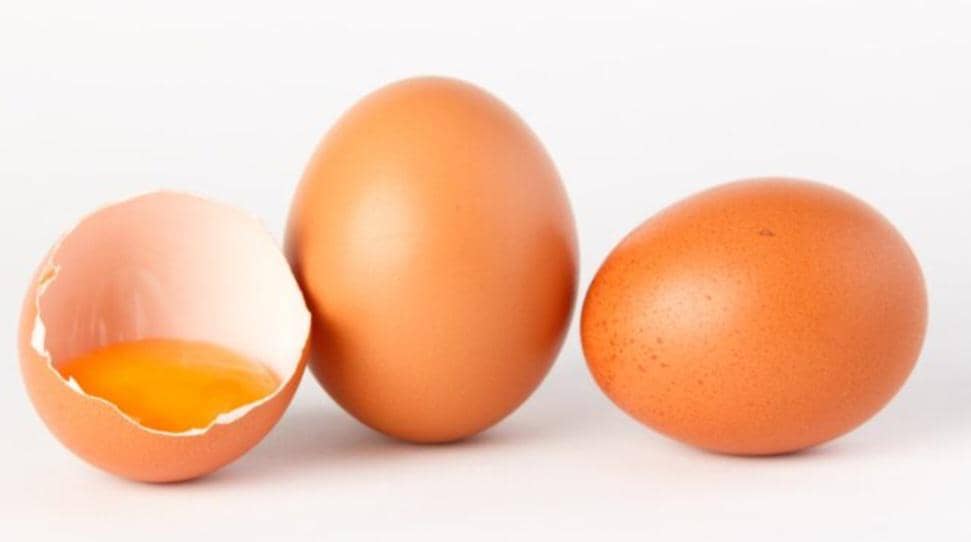 Tiga butir telur ayam negeri berwarna cokelat, satu di antaranya pecah memperlihatkan kuning telur di atas latar putih.