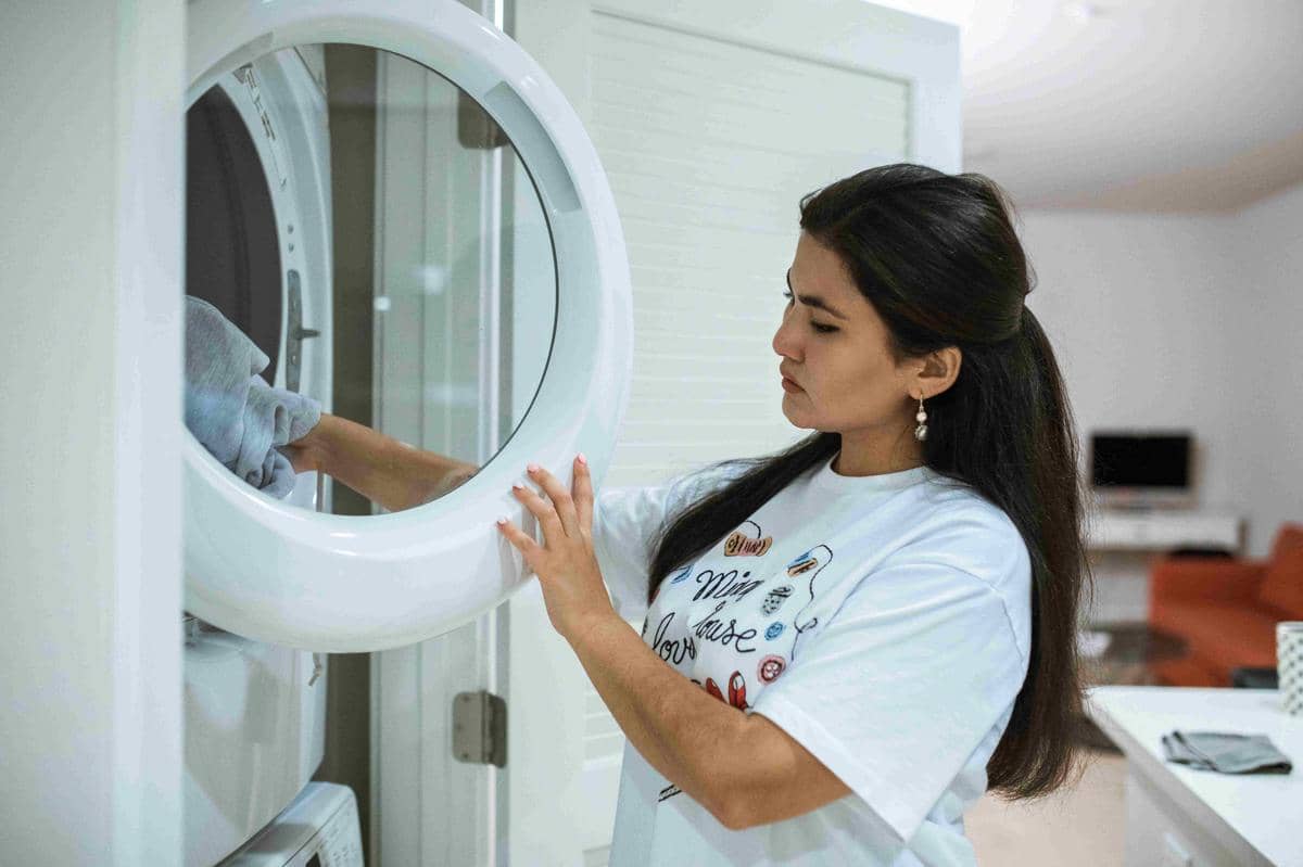 Seorang wanita memasukkan pakaian ke dalam mesin cuci di ruang laundry modern dengan pencahayaan terang.