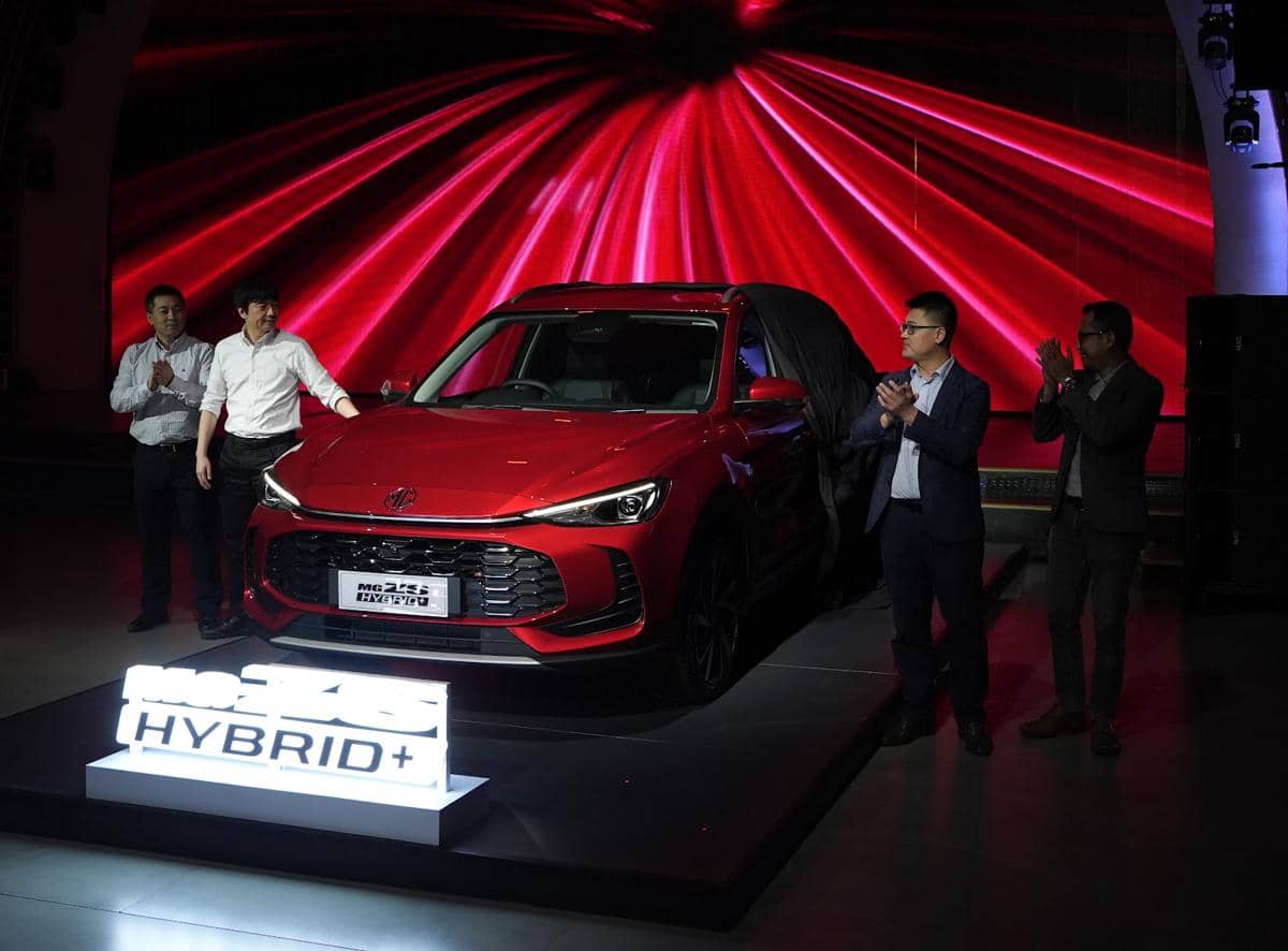 Peluncuran mobil MG ZS Hybrid+ berwarna merah dengan latar belakang cahaya merah dan beberapa orang berdiri di sekitarnya.