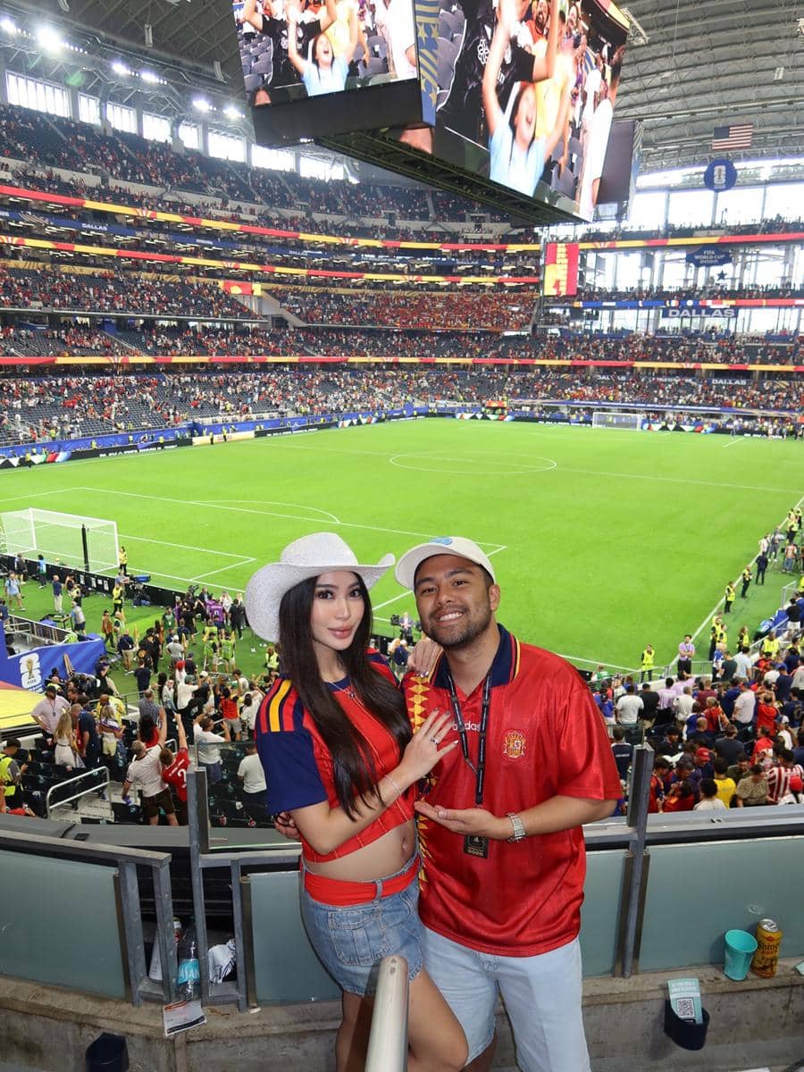 Sepasang penonton mengenakan jersey tim Spanyol berpose di tribun stadion besar saat pertandingan Spanyol melawan Prancis berlangsung.