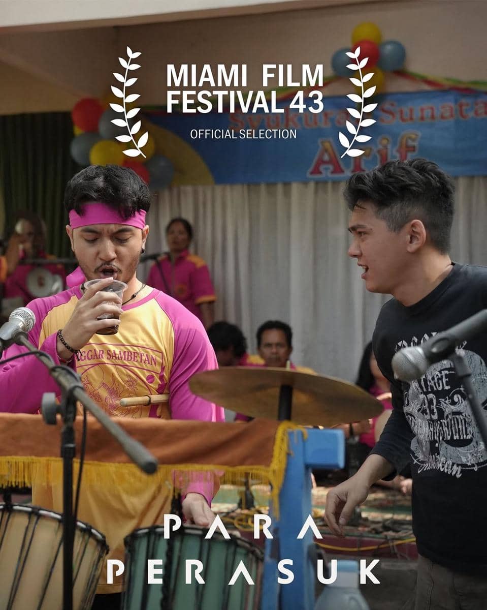 Dua pria sedang tampil di atas panggung dengan alat musik perkusi, mengenakan pakaian kasual dan seragam berwarna cerah dalam suasana festival.