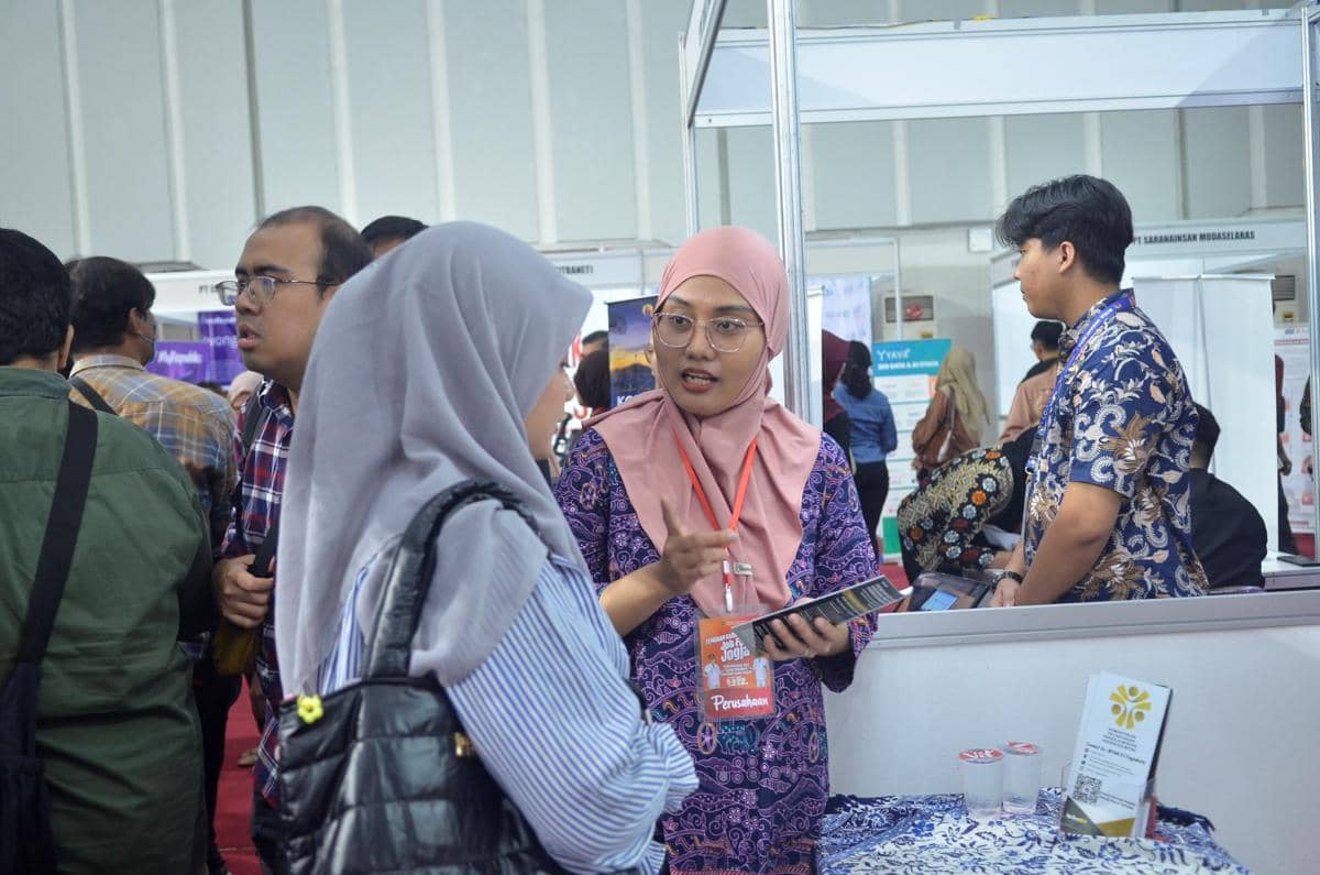 Seorang petugas mengenakan hijab pink berbicara dengan pengunjung di stan pameran bursa kerja Kota Yogyakarta 2026.