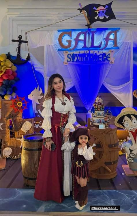 Seorang wanita dan anak kecil mengenakan kostum bajak laut berwarna merah dan putih berpose di pesta ulang tahun bertema bajak laut ke-6 Gala Sky.