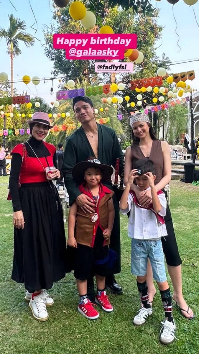 Sekelompok orang dewasa dan anak-anak berpose bersama di pesta ulang tahun bertema luar ruangan dengan dekorasi balon warna-warni.