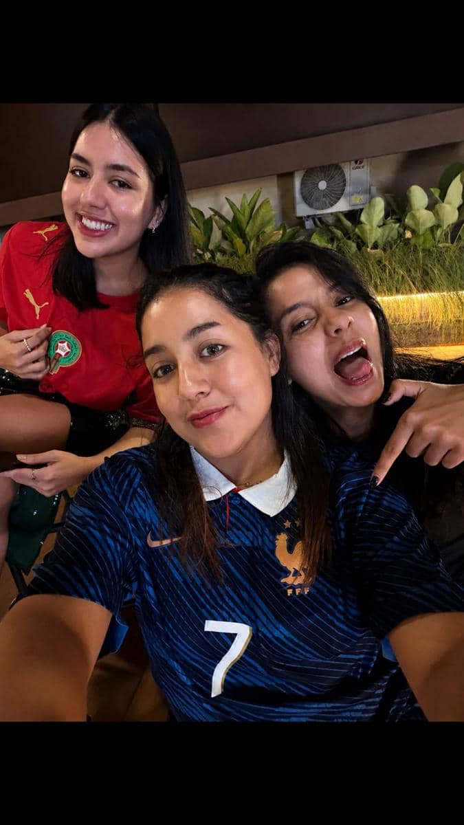 Tiga perempuan berpose bersama mengenakan jersey tim nasional berbeda saat menonton bareng Piala Dunia 2026 di sebuah tempat santai.