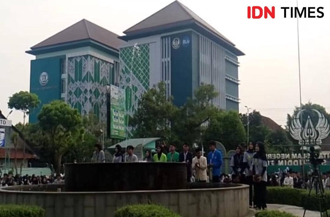 Mahasiswa berkumpul di halaman kampus UIN Saizu Purwokerto dengan latar gedung utama berarsitektur modern dan pepohonan rindang.